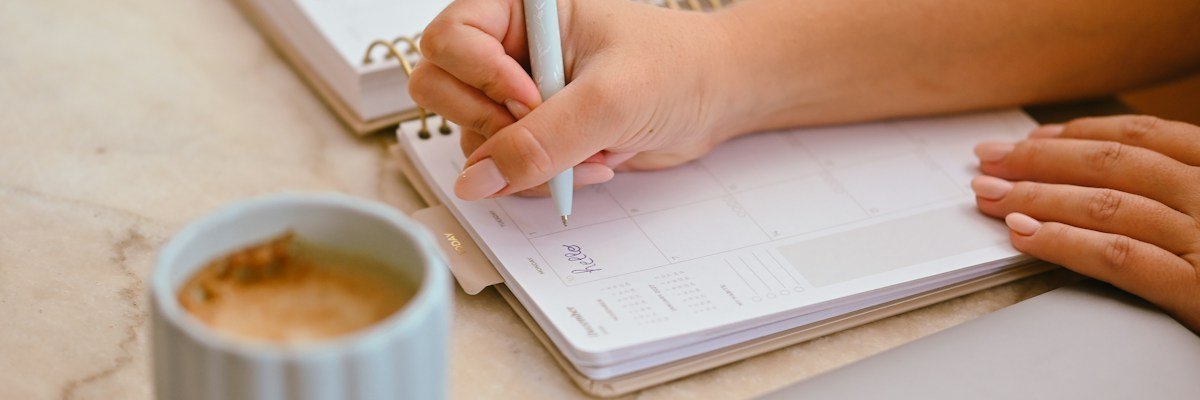 コーヒーの横で手帳に書き込む女性の手元