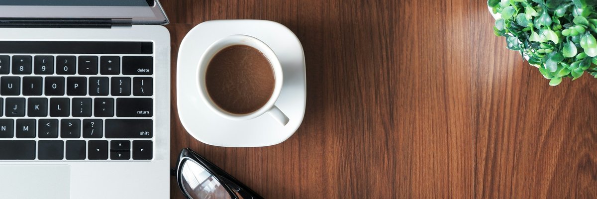 木のデスクに置かれたノートパソコンとコーヒー